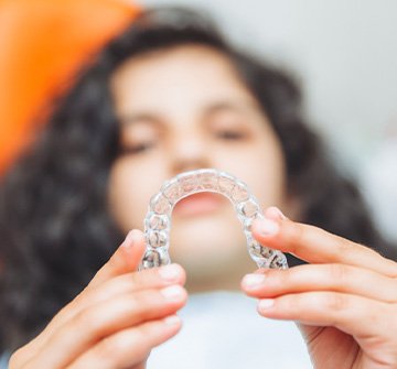 Teenage girl smiling while holding aligner in treatment chair