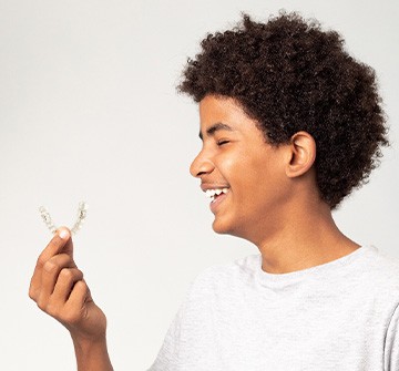 Teenager smiling while holding clear aligner