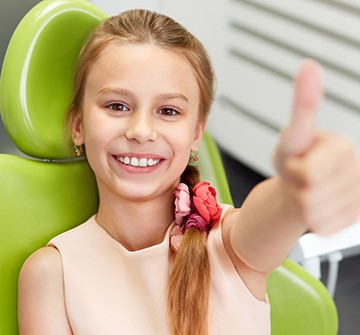 Little girl in dental chair giving thumbs up