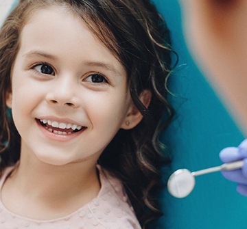 A little girl sitting in the dentist’s chair while smiling at her dentist who provides filling for kids in Fitchburg