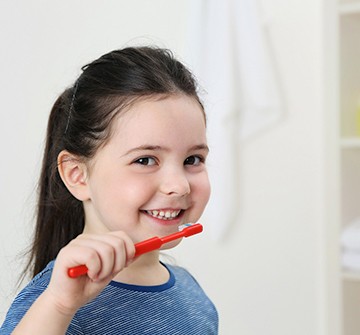 young girl smiling while brushing her teeth