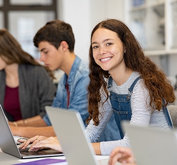 Teen girl smiling while working on computer at school
