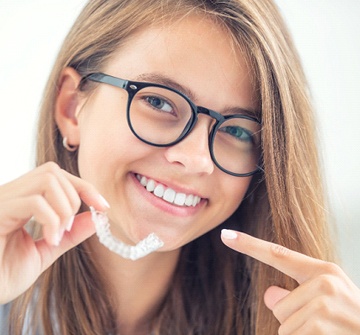 A young, female teen holding a clear aligner