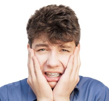 A teenage boy wearing a blue shirt and cringing in pain while wearing braces