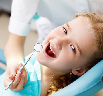 A young girl with red hair smiling while receiving a dental checkup and cleaning