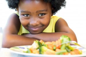 little girl smiling with plate of vegetables 