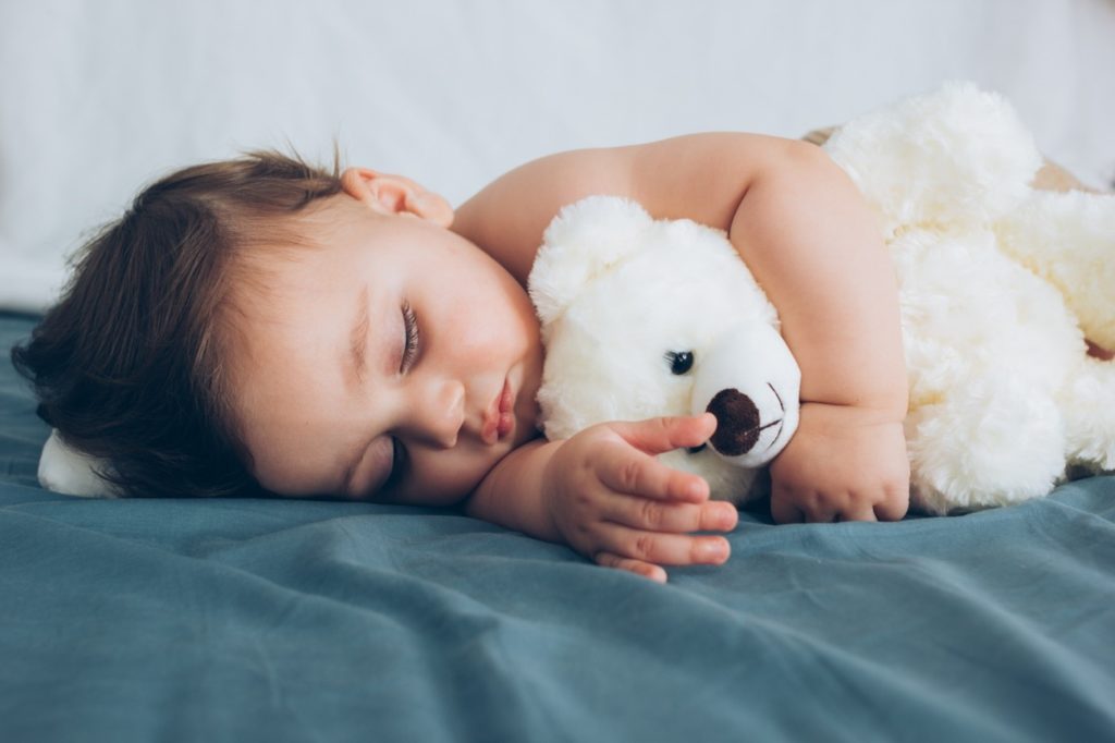 Closeup of baby sleeping on bed with stuffed animal